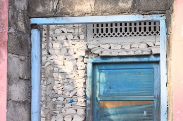 Blue wooden door in a stone wall of an abandoned pink house (Ari Atoll, Maldives)