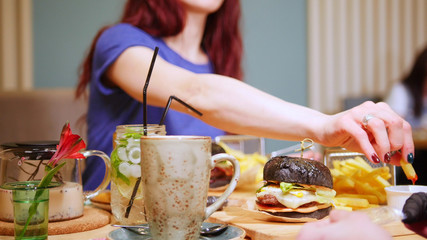 A couple sitting by table in a cafe. A woman eating fries with sauce