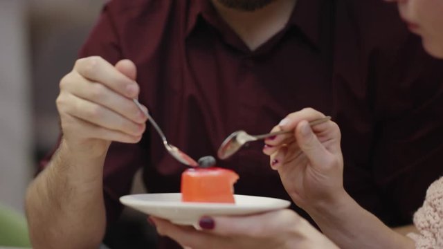 Husband and wife are feeding each other with a heart shaped cake in a cafe
