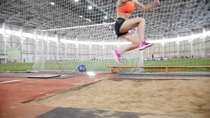 Young blonde woman running and performing a long jump in the sports arena