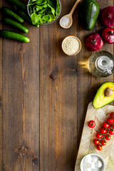 Ingredients for fresh vegetable salad and cutting board on dark wooden kitchen desk top view copy space