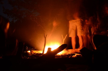 Picnic in the night forest. People are standing around a fire