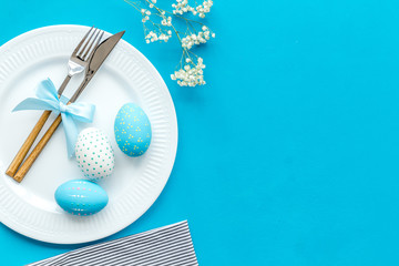 Easter table decoration in blue colors. Plate, cutlery, painted eggs and dry white flowers,...