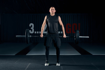 Young man with barbell flexing muscles and making shoulder press lunge in gym