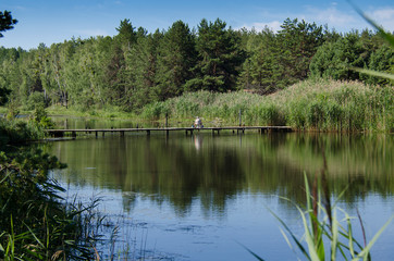 Wooden bridge over the River in the forest, where a fisherman sits amid green forests and blue sky