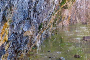 Raindrops flow down from the rocks in a mountain lake. Beautiful rocks cave with moss, close-up view.