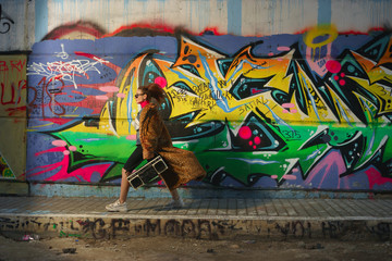 Photo of young hip hop girl walking  against graffiti wall with boombox 