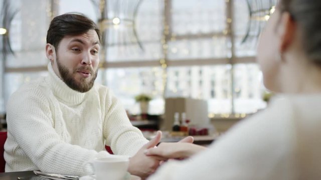 Happy adult man is holding female hand with a snile on his face while sitting in a cafe