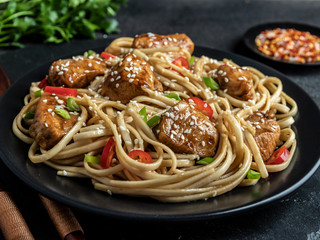 Asian noodles with chicken teriyaki , sesame, rustic stone background. Closeup. Chinese/Japanese noodles