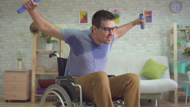 strong paralyzed male wheelchair athlete in sweat doing dumbbells