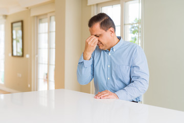 Middle age man sitting at home tired rubbing nose and eyes feeling fatigue and headache. Stress and frustration concept.