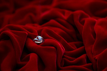 Golden engagement ring with diamond. Special jewelry design. Red soft velor fabric in folds and drapes. The wedding ring is in red fabric.