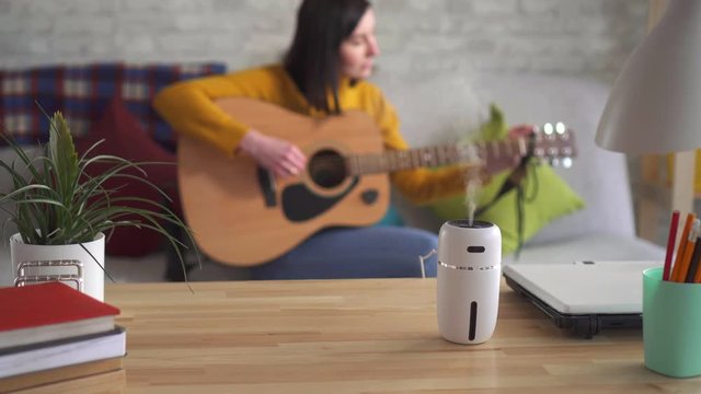 Young woman tuning guitar in the foreground ultrasonic humidifier