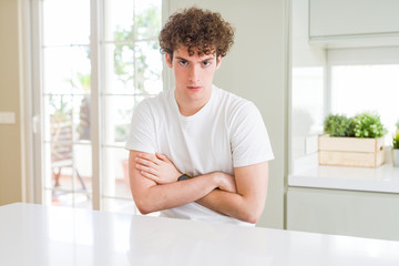 Young handsome man wearing white t-shirt at home skeptic and nervous, disapproving expression on face with crossed arms. Negative person.