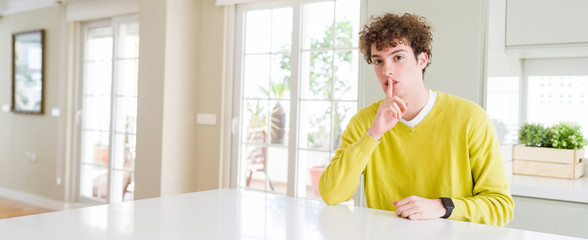 Wide angle shot of young handsome man at home asking to be quiet with finger on lips. Silence and secret concept.