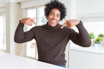 African American man wearing winter sweater looking confident with smile on face, pointing oneself...