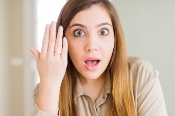 Beautiful young woman showing engagement ring on hand scared in shock with a surprise face, afraid and excited with fear expression