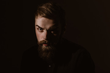 Sepia portrait of a stylish man with a beard and stylish hairdo dressed in the black shirt on the dark background