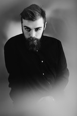 Obraz premium Black and white photo of a stylish man with a beard and stylish hairdo dressed in the black shirt stands in the fog
