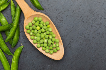 Green, tender, fresh and raw peas. Close-up and top view. Rustic appearance. Rustic appearance and wooden spoon. Black background.