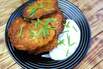 Potato pancakes with sour cream on a black plate