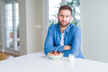 Handsome man eating cereals for breakfast at home skeptic and nervous, disapproving expression on face with crossed arms. Negative person.