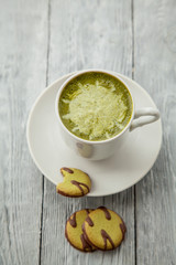 cup of matcha green tea latte and some cookies on grey wooden background