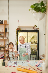 Portrait of smiling mature woman creating flower compositions with cute girl in art studio, copy space