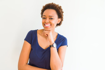 Young beautiful african american woman over white background looking confident at the camera with smile with crossed arms and hand raised on chin. Thinking positive.