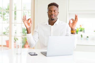 African american business man working using laptop relax and smiling with eyes closed doing meditation gesture with fingers. Yoga concept.