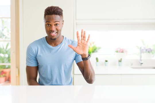 Handsome african american man wearing casual t-shirt at home showing and pointing up with fingers number five while smiling confident and happy.