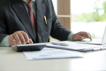 Businessman analyzing investment charts on desk office and using a laptop to calculate about profit or lost in his office. Finance accounting concept