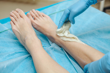 Fototapeta premium Epilation wax in the spa salon. Beautician imposes wax on women's legs. Close-up.