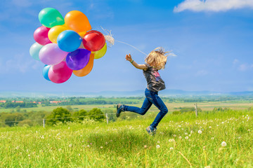 Glückliches Mädchen spring mit vielen bunten Luftballons über eine grüne Wiese - 254750048