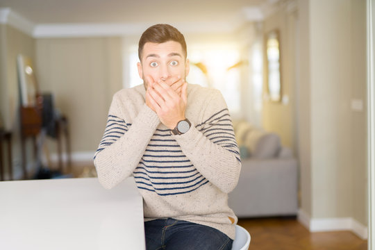 Young handsome man wearing a sweater at home shocked covering mouth with hands for mistake. Secret concept.
