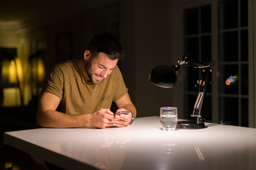 Young handsome man studying at home , using smartphone, looking at the phone smiling