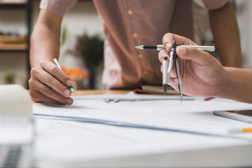 Hands of architect or engineer using drawing compass with blueprint on desk in office.Team of architects engineer discussing and check documents and business workflow.Construction concept.