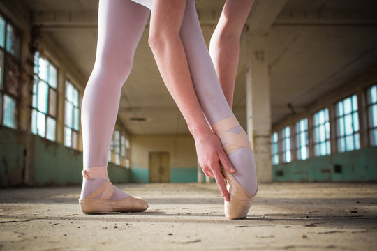 Ballerina Dancing In An Old Building. Close Up Photo Of Young, Elegant, Graceful Woman Ballet Dancer Preparing Her Pointe Shoes
