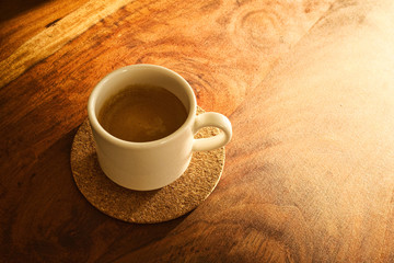 Cup of espresso on a wooden plate in low sunlight. Place for text