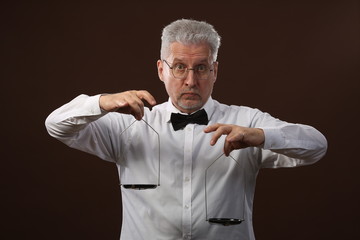Elderly gray-haired man 50s, in white shirt, glasses and bow tie weighing something on scales with kettlebells