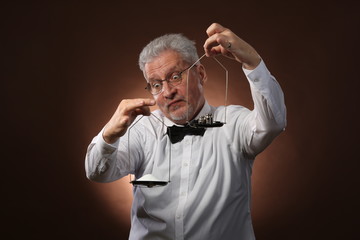Elderly gray-haired man 50s, in white shirt, glasses and bow tie weighing something on scales with kettlebells