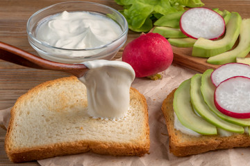Preparation of a toast with  yogurt, avocado and radish. Close up. Soft focus.