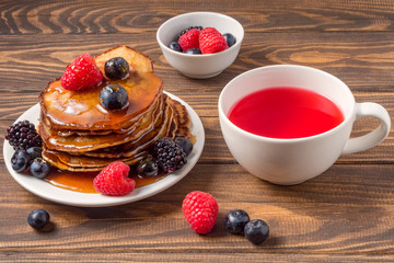 Pancakes with blueberries and strawberries and cup of red juice on wooden background