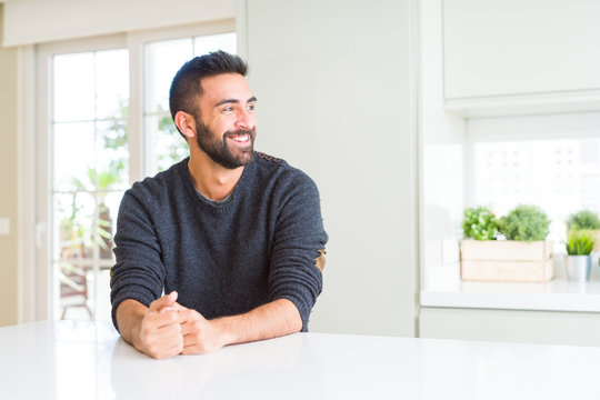 Handsome hispanic man wearing casual sweater at home looking away to side with smile on face, natural expression. Laughing confident.