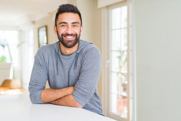 Handsome hispanic man wearing casual sweatshirt at home happy face smiling with crossed arms looking at the camera. Positive person.