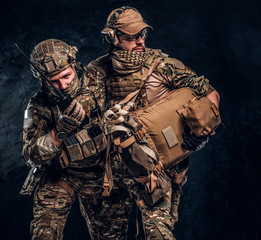 Combat conflict, special mission, retreat. Military medic rescues his wounded teammate carrying him off the battlefield. Studio photo against a dark wall