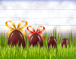 Chocolate Easter eggs with ribbon bows on white rustic wooden background with grass. Copy space.