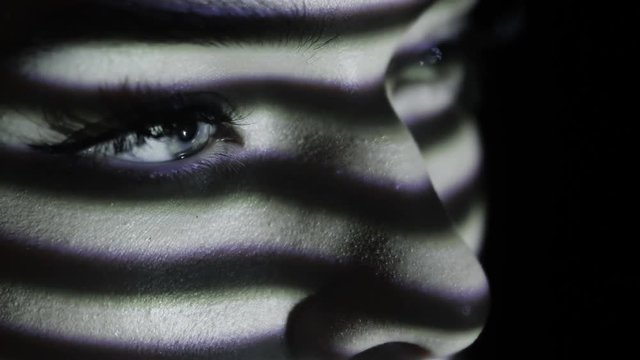Projection of black and white lines on girl&rsquo;s face. Close up eyes of girl with an abstract pattern of lines and red lips on her face. Illumination from the blinds in the room. Concept. Sharp look.