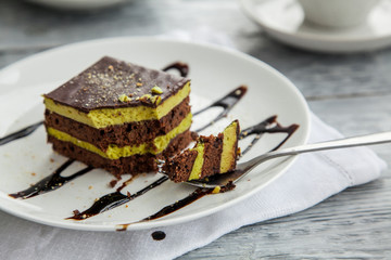 a portion of a three-layer chocolate cake with a broken piece on a plate