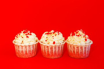 Three cupcakes with delicate white cream on a red background